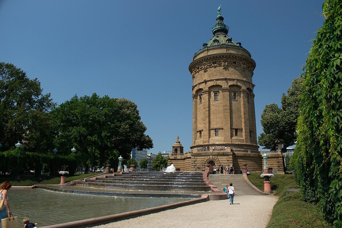 Wasserturm am Friedrichsplatz: runder Turm aus Sandstein mit grüner Kuppel, davor Wasserbecken, Treppen und Bäume